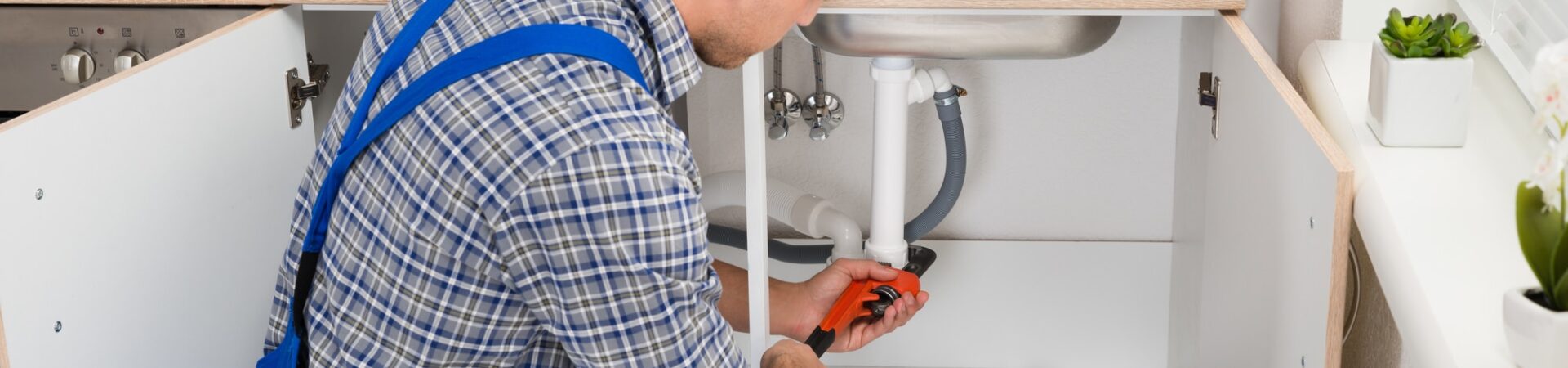 Male Plumber Fixing Sink Pipe With Adjustable Wrench In Kitchen